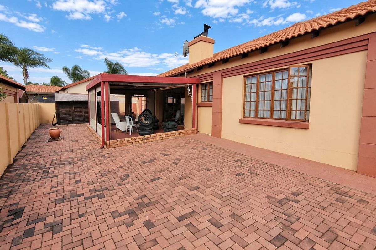 Rear exterior view featuring a paved courtyard, a covered patio area, and a traditional house facade with terracotta roof tiles.
