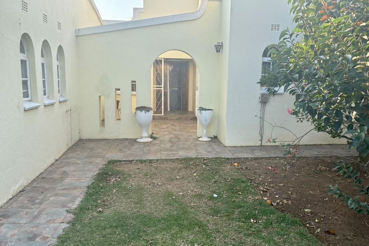 Rear exterior view featuring a tiled patio area, arched entryway with security gate, and plastered walls with arched windows.