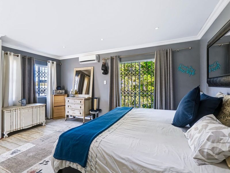 A spacious bedroom featuring tiled flooring, recessed downlighting, and a wall-mounted split-system air conditioner, with security gates on the windows and sliding door.