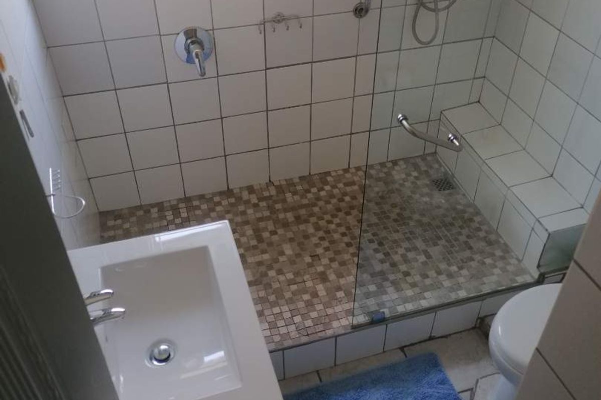 Compact bathroom featuring a walk-in shower with mosaic tile flooring, glass partition, wall-mounted shower head, and a modern vanity basin.