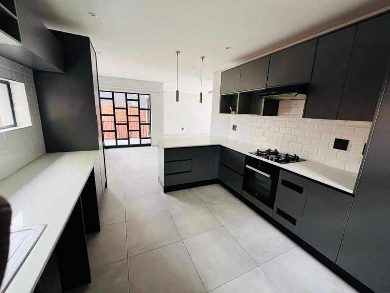 Modern open-plan kitchen featuring dark cabinetry, stone countertops, subway tile backsplash, and integrated appliances, flowing into a bright living area with large glass doors.