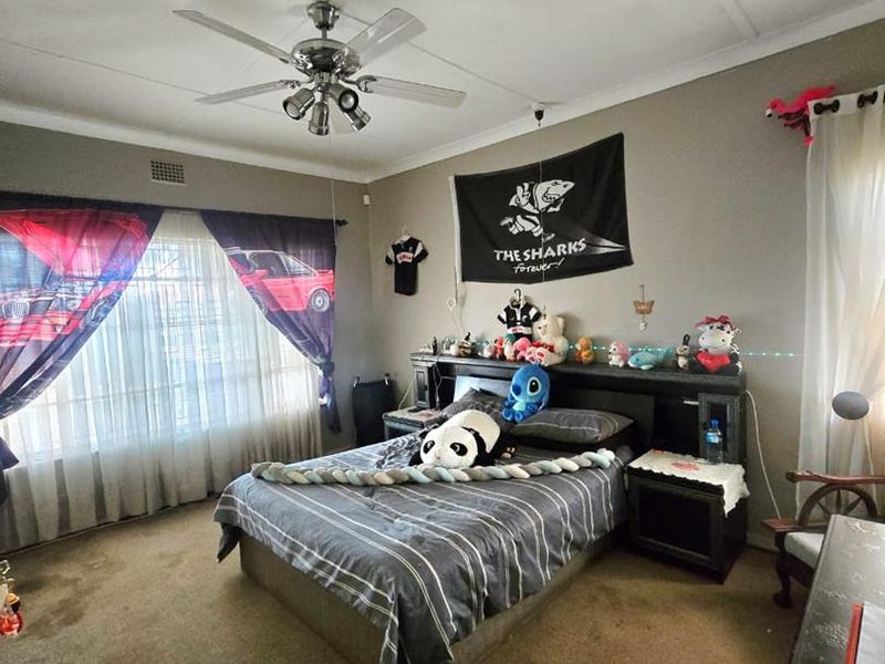 A bedroom featuring a ceiling fan, built-in headboard, and large windows. The room requires cosmetic updates including new flooring and ceiling repairs.