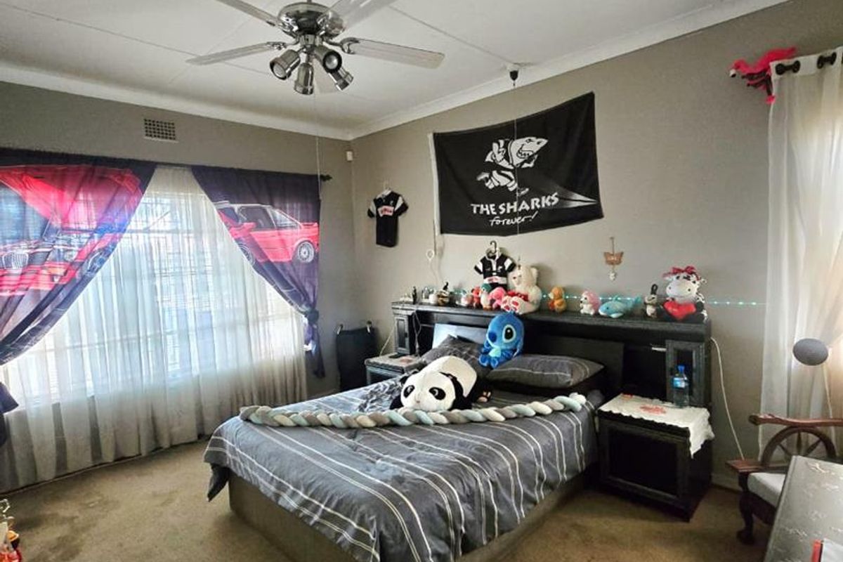 A bedroom featuring a ceiling fan, built-in headboard, and large windows. The room requires cosmetic updates including new flooring and ceiling repairs.