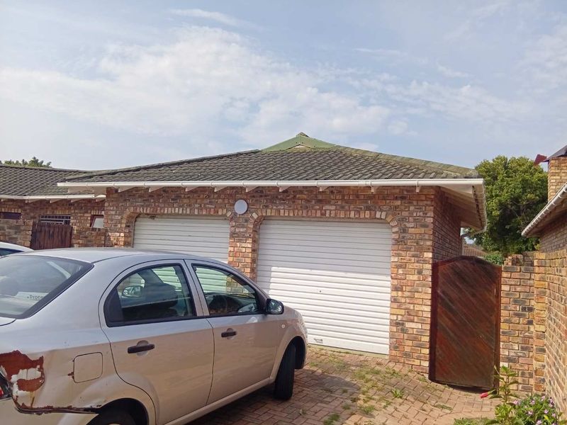A double garage featuring face brick construction, white roller doors, and a tiled roof, situated with a paved driveway and side access gate.