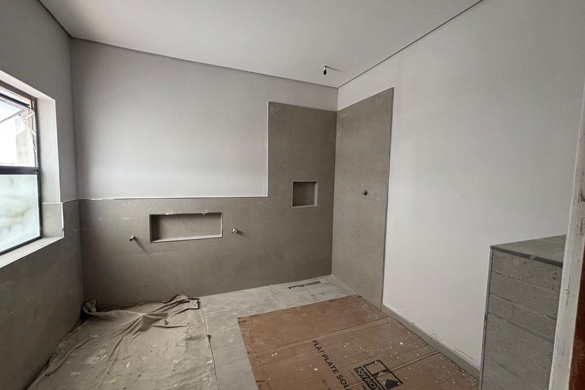 An unfinished bathroom space featuring tiled shower walls with built-in niches and exposed plumbing rough-ins, ready for final fixtures and completion.