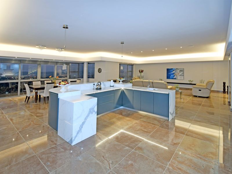 Spacious open-plan living area featuring a modern marble kitchen island, high-end stone flooring, and expansive windows with integrated recessed lighting throughout.