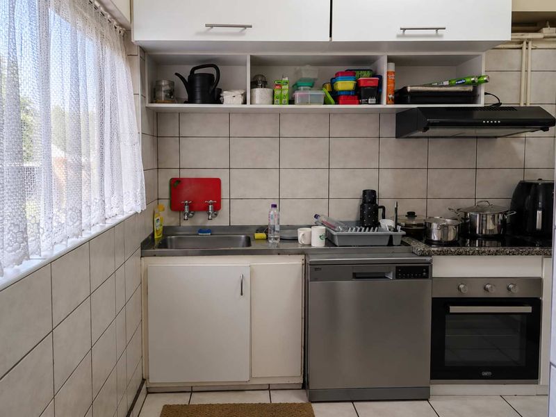 Compact kitchen featuring built-in cabinetry, stainless steel sink, integrated dishwasher, and built-in oven with extractor fan, finished with tiled backsplash and flooring.