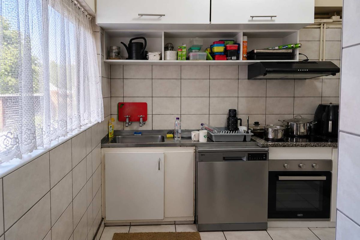 Compact kitchen featuring built-in cabinetry, stainless steel sink, integrated dishwasher, and built-in oven with extractor fan, finished with tiled backsplash and flooring.
