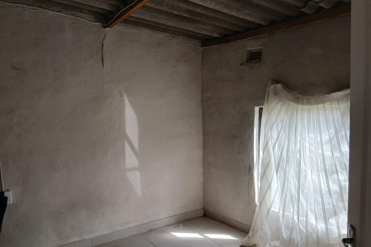 An empty bedroom featuring tiled flooring and exposed corrugated roof sheeting, requiring significant renovation and finishing to improve the overall condition.