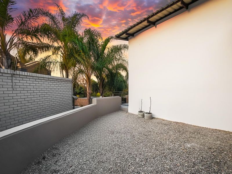 A clean, low-maintenance rear outdoor area featuring a gravel surface, painted boundary walls, and a modern roof overhang at sunset.