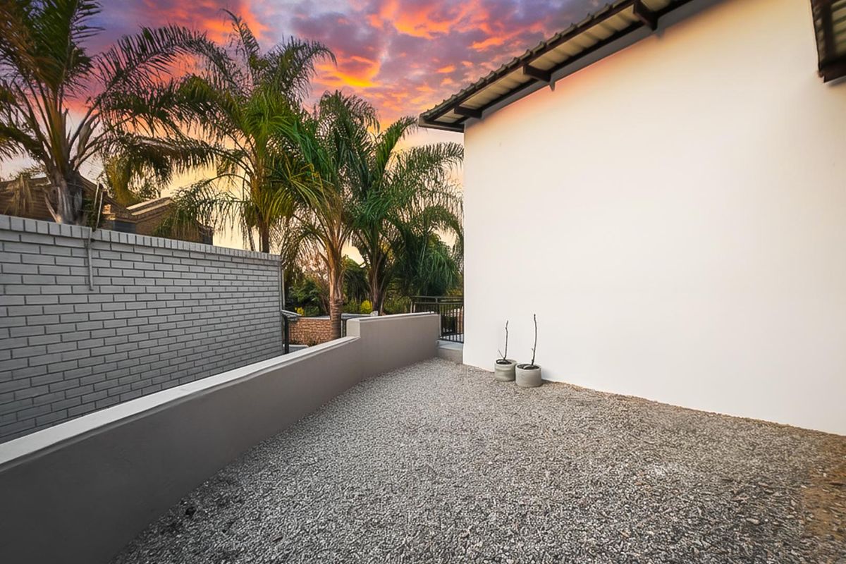 A clean, low-maintenance rear outdoor area featuring a gravel surface, painted boundary walls, and a modern roof overhang at sunset.
