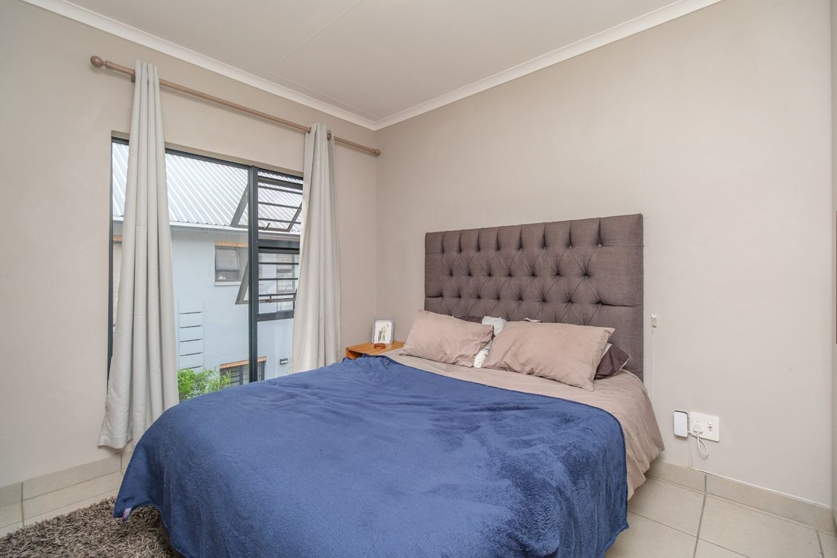 A well-maintained bedroom featuring neutral wall tones, tiled flooring, and a large window providing natural light.