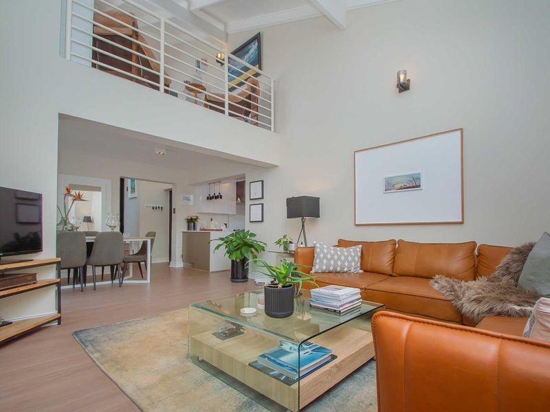 Spacious open-plan living area featuring a double-volume ceiling, mezzanine level with metal balustrade, and modern laminate flooring throughout.