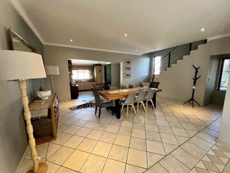 Spacious open-plan dining area featuring tiled flooring, recessed lighting, and a staircase with a modern metal balustrade, leading through to the kitchen.