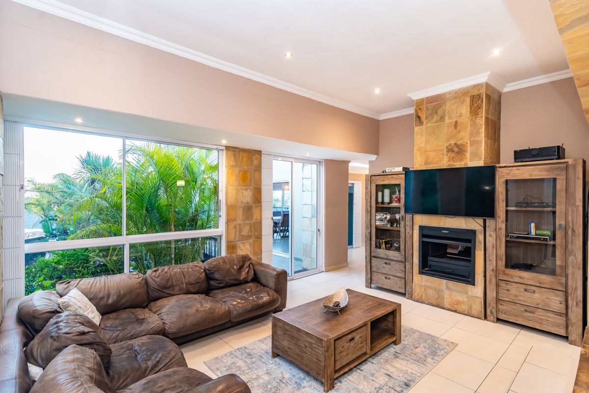 Spacious living room featuring a stone-clad fireplace, large picture windows with garden views, and tiled flooring, providing a bright and comfortable atmosphere.
