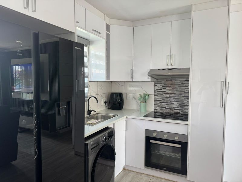 Compact modern kitchen featuring white high-gloss cabinetry, stone countertops, integrated oven, electric hob, and a stylish tiled backsplash.