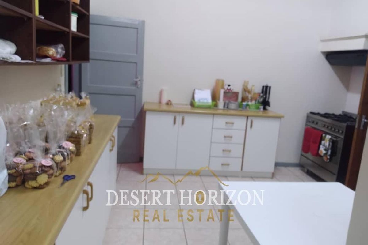 A functional kitchen featuring white cabinetry, laminate countertops, a gas stove with extractor fan, and tiled flooring.