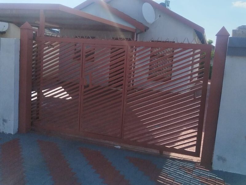 Front view of the property featuring a metal security gate, paved driveway, and an attached carport.