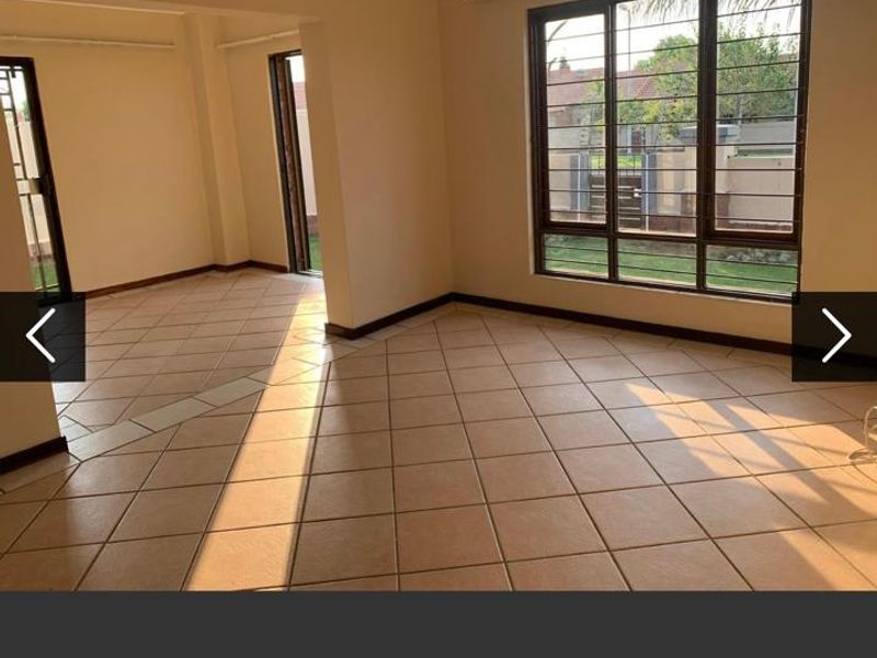 A bright, empty living area featuring neutral tiled flooring, large windows with security bars, and direct access to the exterior through sliding doors.