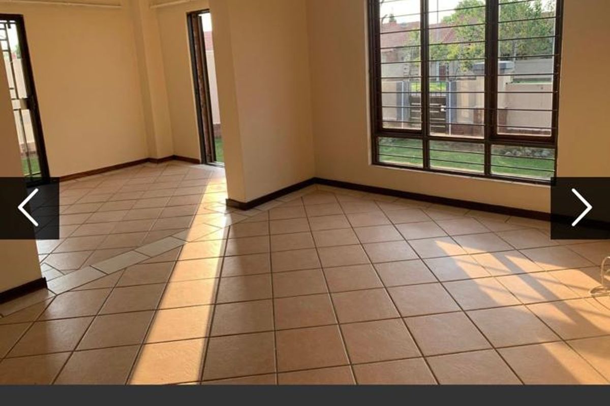 A bright, empty living area featuring neutral tiled flooring, large windows with security bars, and direct access to the exterior through sliding doors.