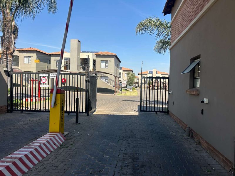 View of the townhouse complex entrance featuring a security boom gate, paved driveway, and perimeter electric fencing.