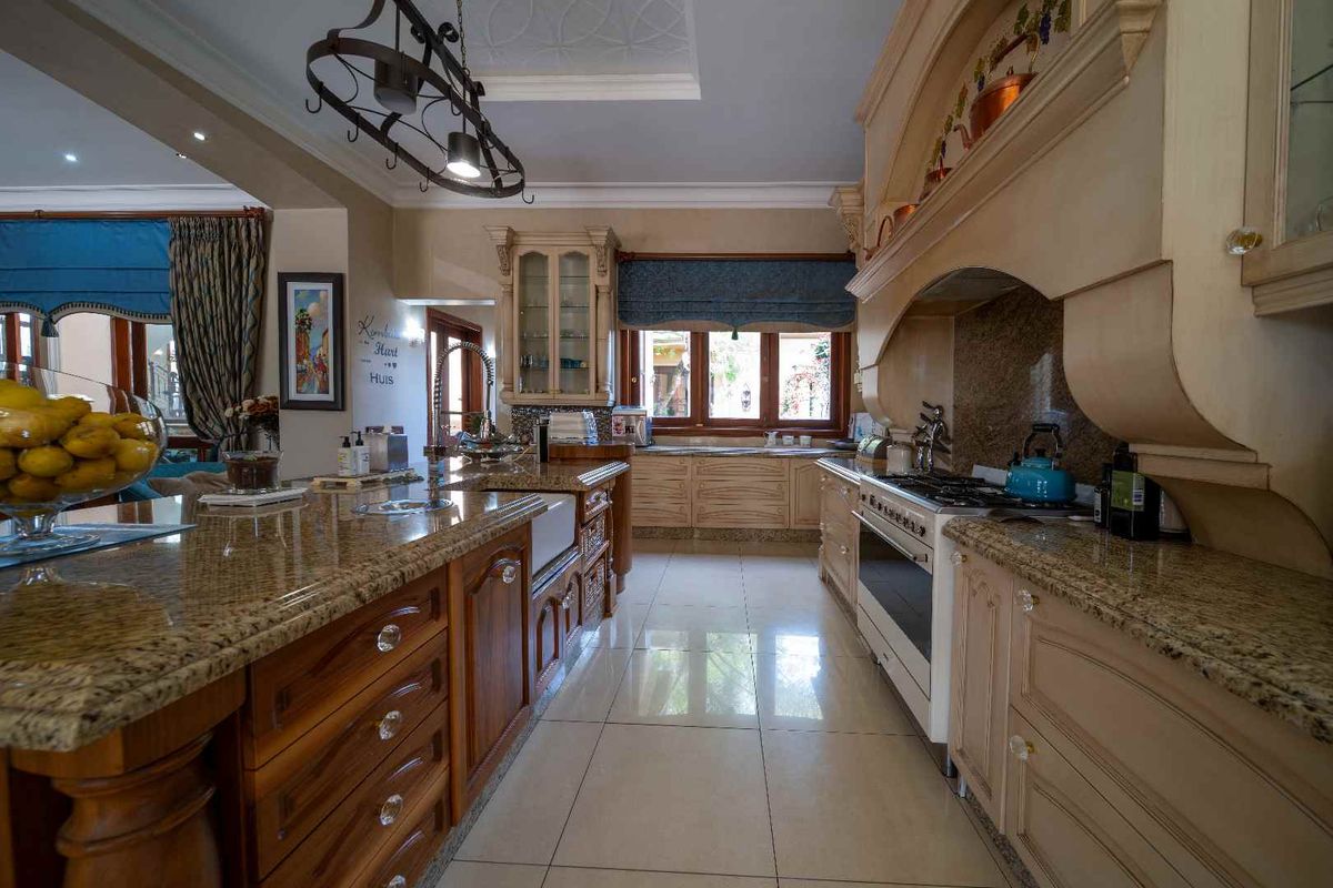 Spacious kitchen featuring granite countertops, a large central island, farmhouse sink, and custom cabinetry with integrated gas stove and extractor hood.