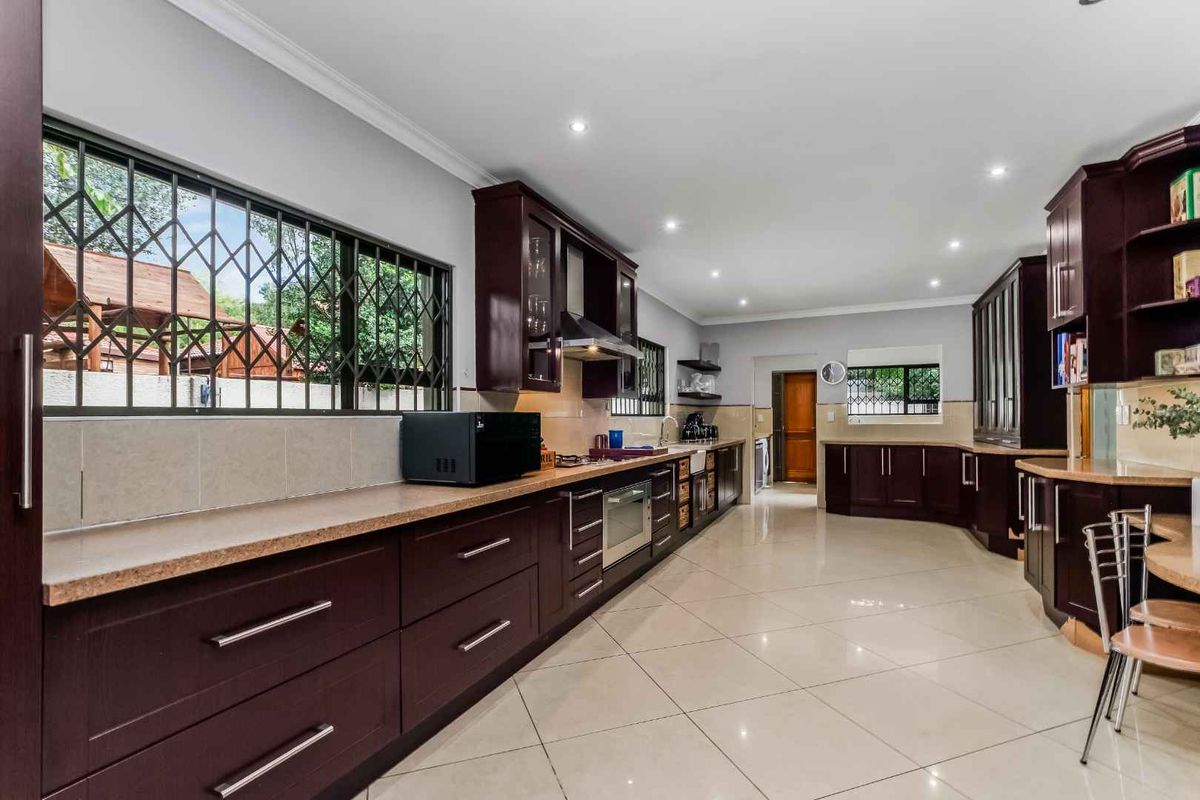 Spacious kitchen featuring dark wood cabinetry, stone countertops, tiled flooring, recessed lighting, and integrated stainless steel appliances.