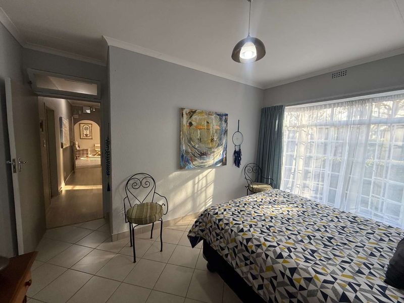 A well-lit bedroom featuring tiled flooring, cove cornicing, and a large window, providing a comfortable and functional living space.