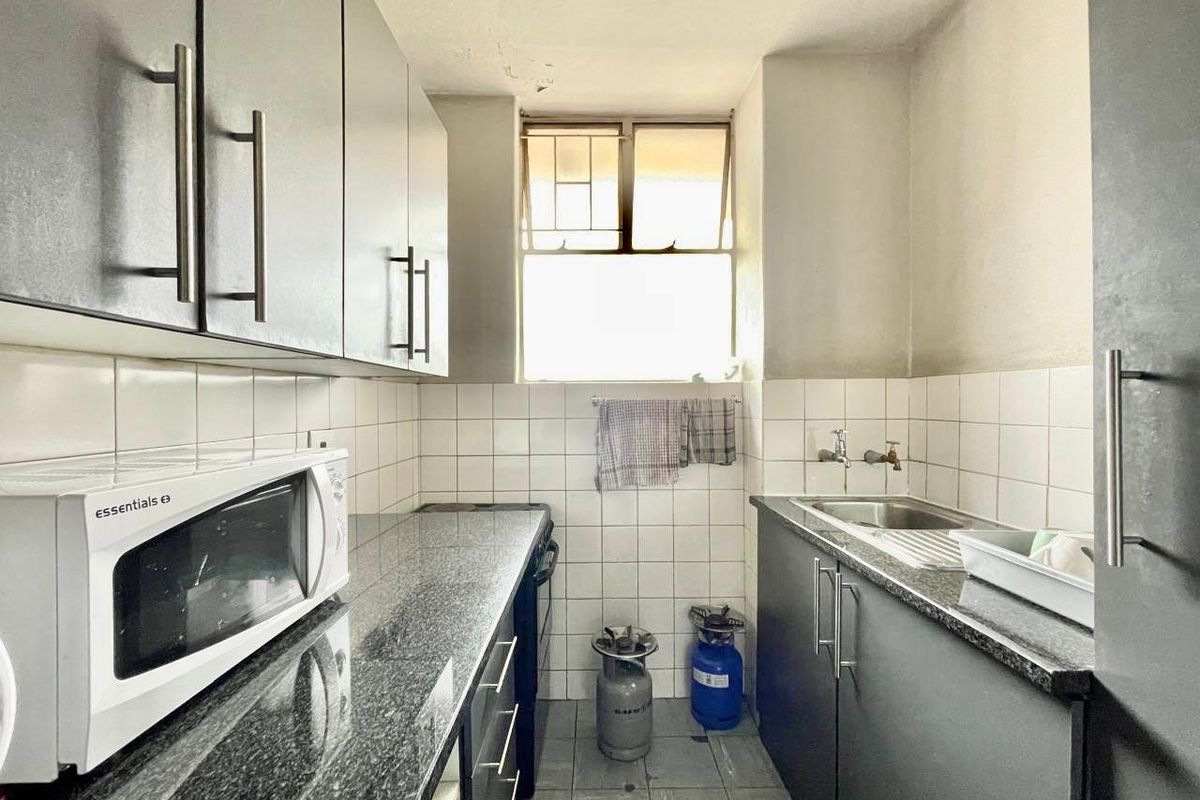 A compact kitchen featuring dark cabinetry, granite countertops, tiled splashbacks, and a stainless steel sink with plumbing connections.