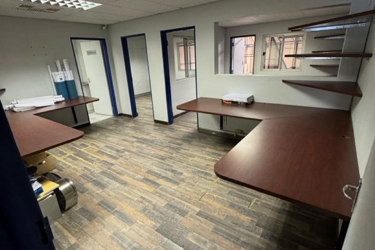 Functional office space featuring built-in corner desks, wall-mounted shelving, suspended ceiling with recessed lighting, and durable wood-look laminate flooring.