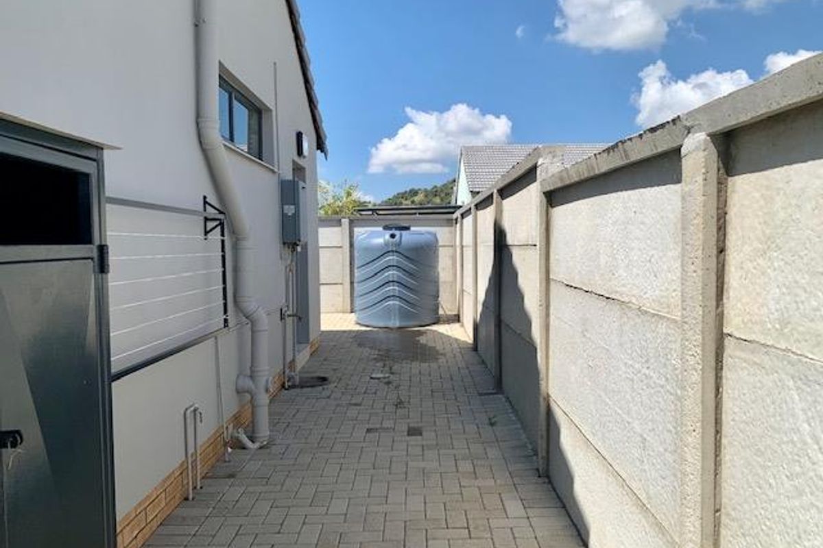 Side exterior passage featuring paved flooring, a water storage tank, wall-mounted washing line, and concrete boundary walling.