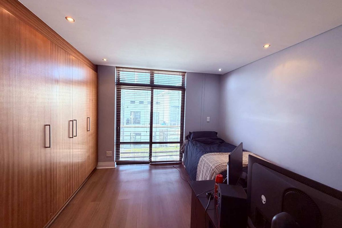 A well-maintained bedroom featuring extensive built-in wooden cabinetry, laminate flooring, and large windows that provide ample natural light.