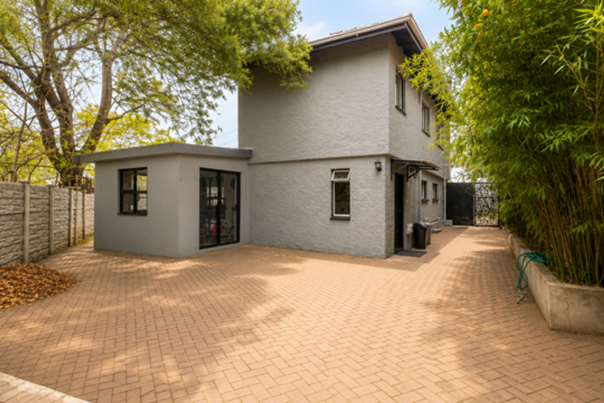 A view of the exterior rear of the townhouse, featuring paved driveway space, a side extension, and established garden borders.