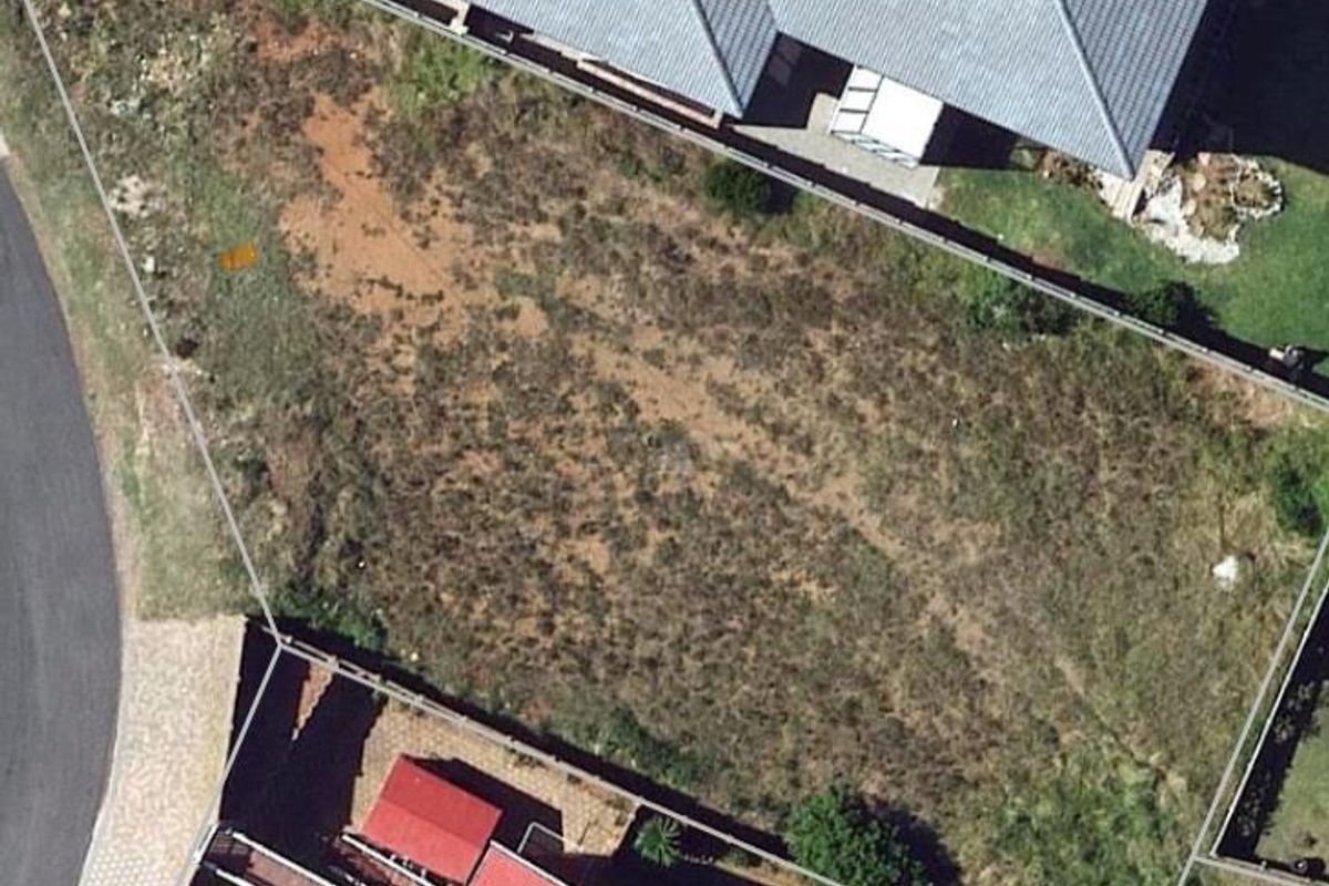 An aerial view of a vacant residential plot, showing the boundary lines, surrounding neighborhood, and existing perimeter fencing.