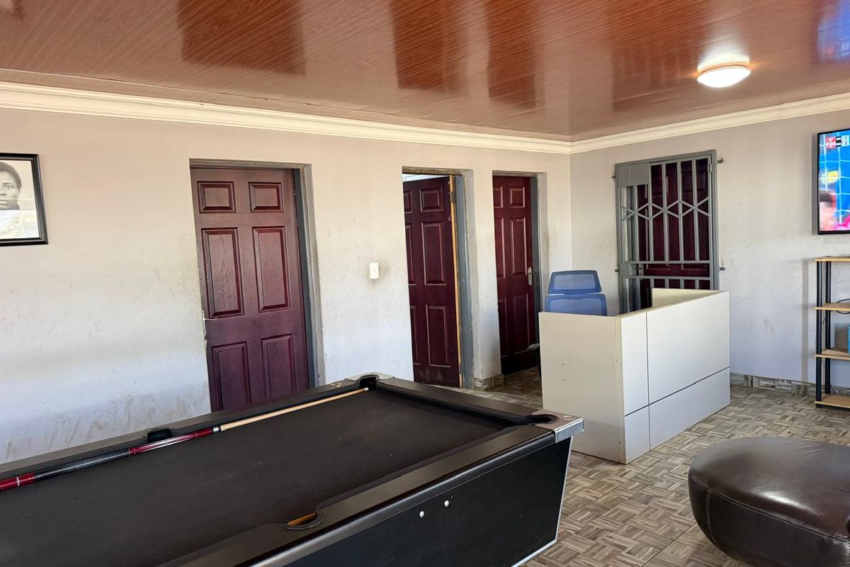 A multi-purpose living area featuring a wooden panel ceiling, tiled flooring, and multiple internal doors with a security gate.