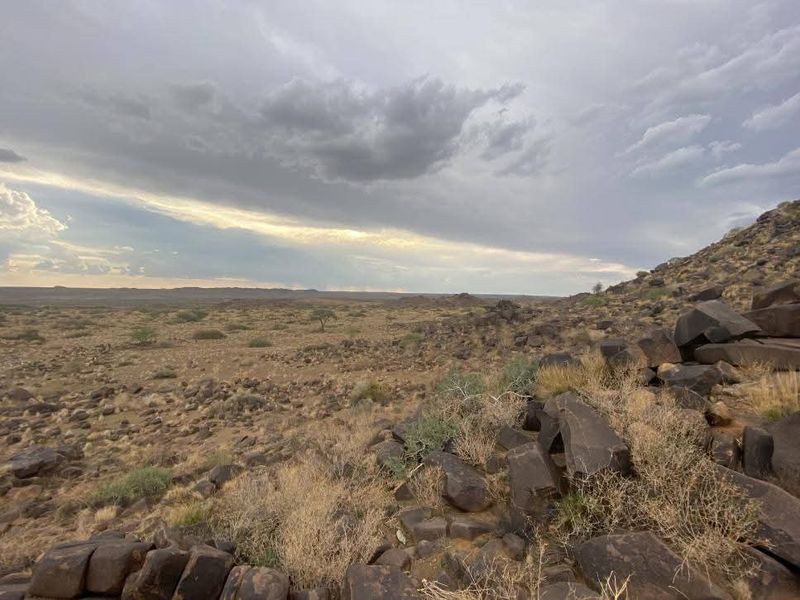 A wide-angle view of the natural landscape featuring rocky terrain and arid vegetation under a cloudy sky.