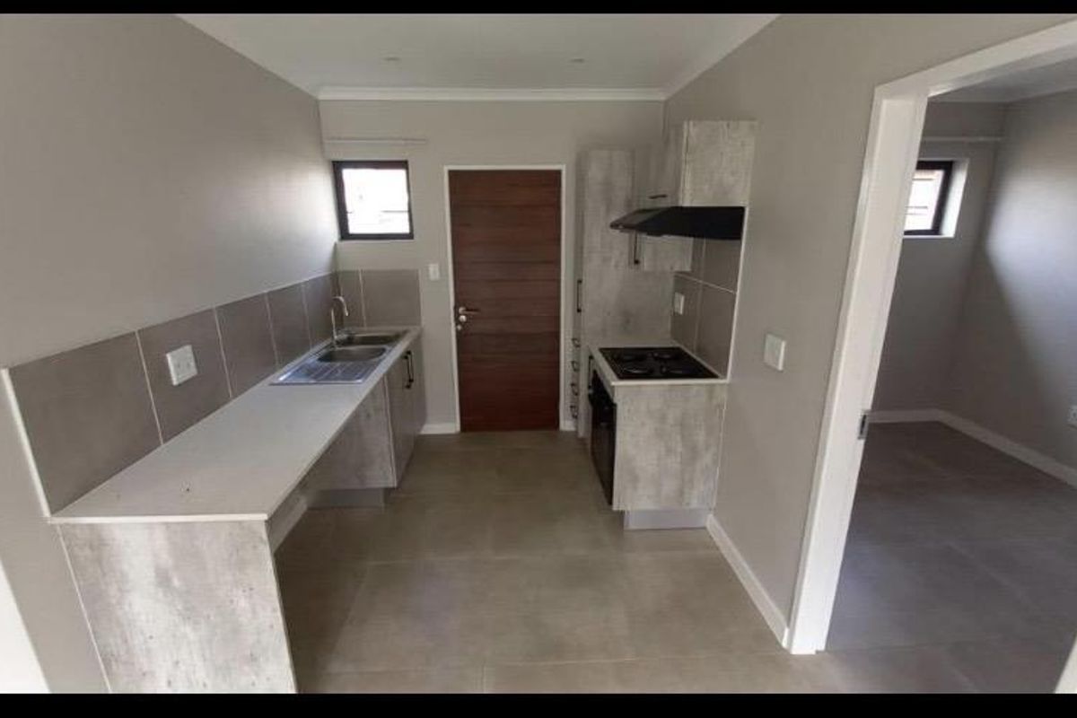 A clean, modern kitchen featuring built-in cabinetry, a stainless steel sink, an electric hob with extractor fan, and neutral tiled flooring.