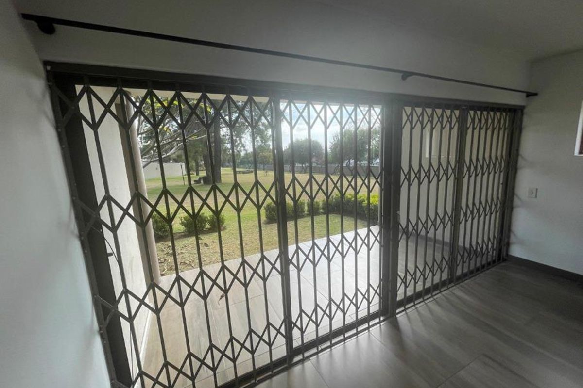 Bright living area featuring large sliding glass doors with a retractable security gate, opening onto a private patio and garden area.