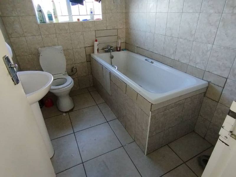 A functional bathroom featuring a pedestal basin, toilet, and a tiled bathtub with wall-to-wall ceramic tiling.