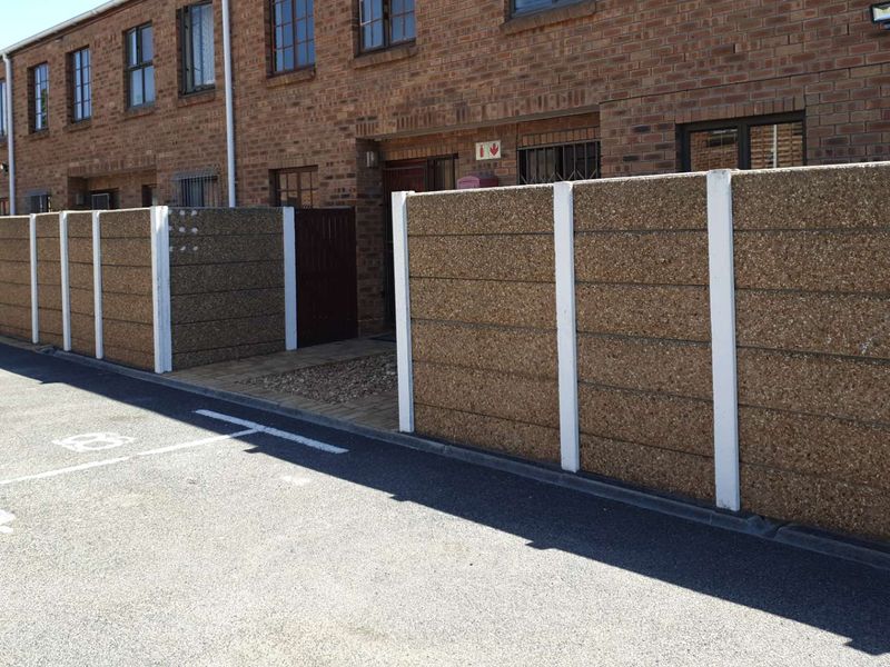 Front exterior view of a townhouse complex featuring brick facade construction and precast concrete boundary walls with paved access paths.