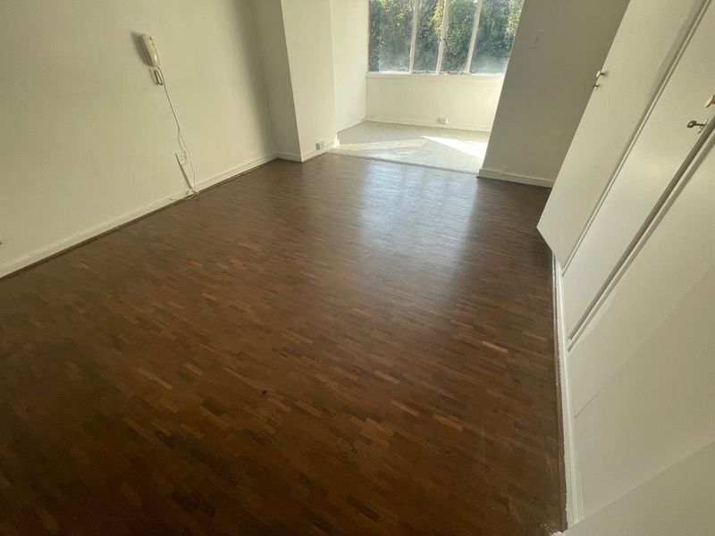 An empty bedroom featuring dark parquet flooring, built-in storage cupboards, and an intercom system, with natural light entering from the adjacent windowed area.