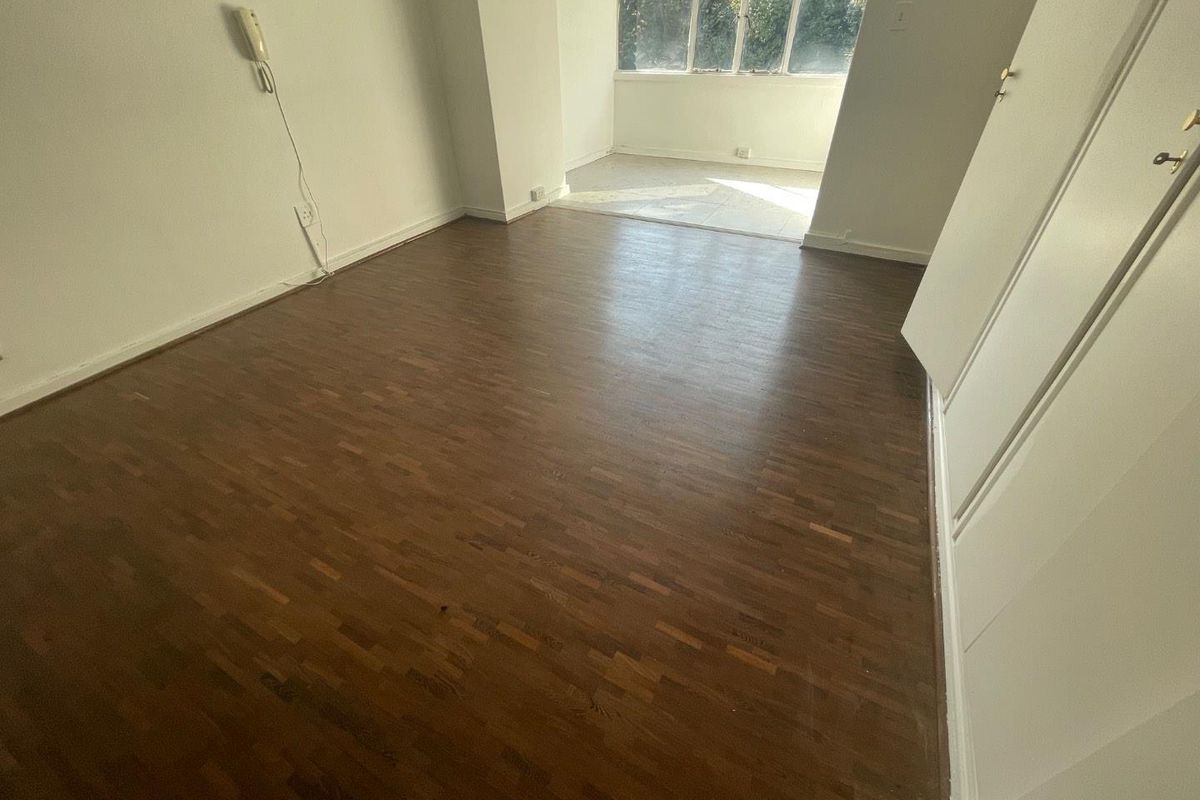 An empty bedroom featuring dark parquet flooring, built-in storage cupboards, and an intercom system, with natural light entering from the adjacent windowed area.