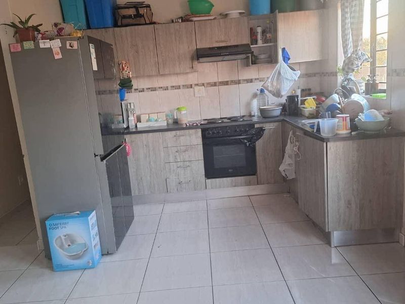 A functional kitchen featuring wood-look cabinetry, built-in oven, extractor fan, tiled backsplash, and ceramic floor tiles.