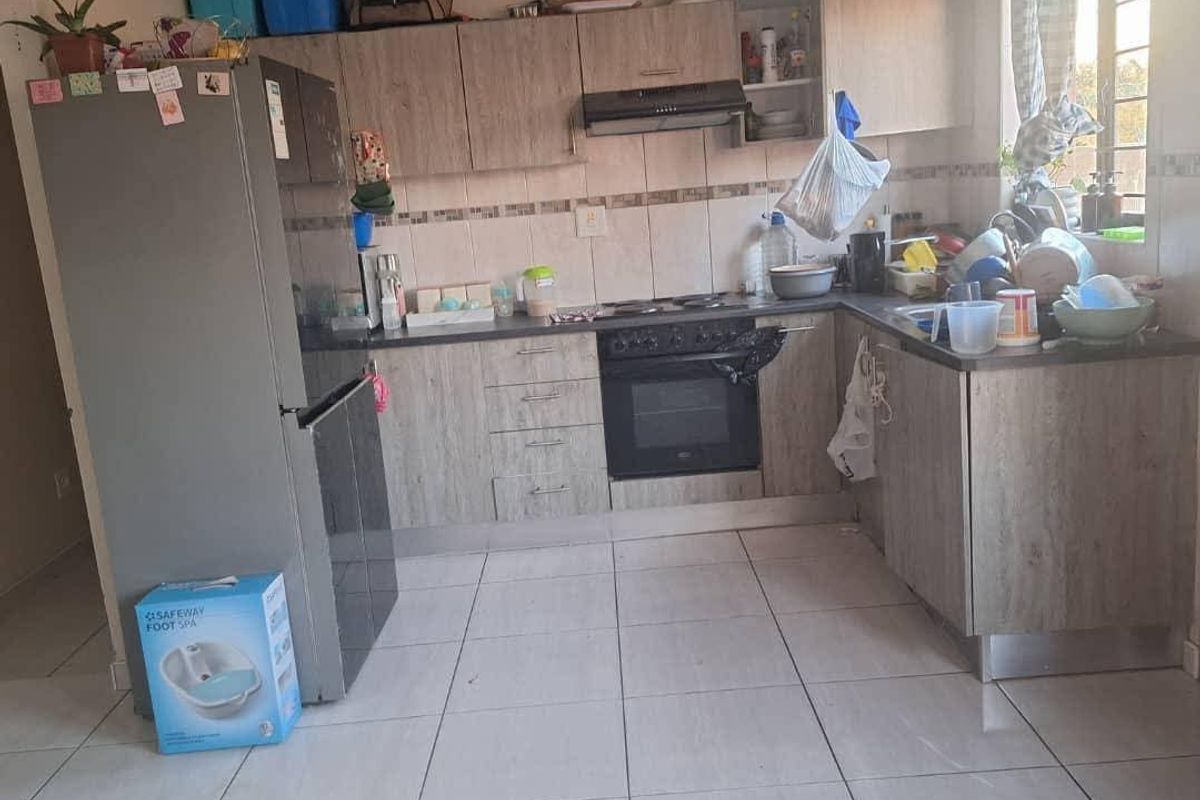 A functional kitchen featuring wood-look cabinetry, built-in oven, extractor fan, tiled backsplash, and ceramic floor tiles.