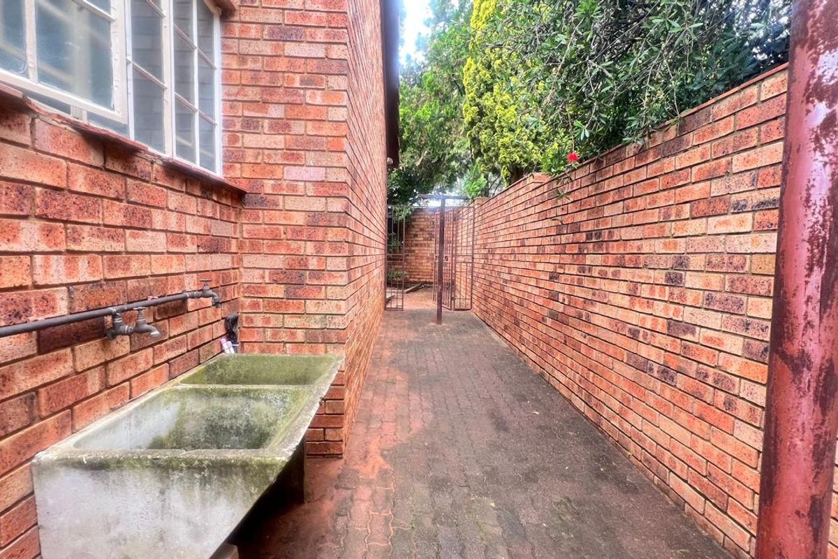 A narrow exterior side passage featuring a brick boundary wall, paved walkway, and a fixed concrete utility sink with plumbing.