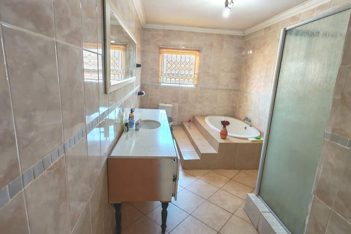 A spacious bathroom featuring a built-in bathtub with tiled steps, a separate shower enclosure, and a vanity unit with a stone countertop.