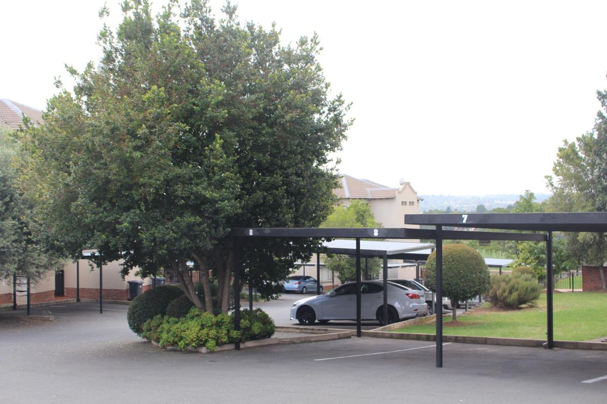 Outdoor parking area featuring covered carports with numbered bays, set within a landscaped residential apartment complex.