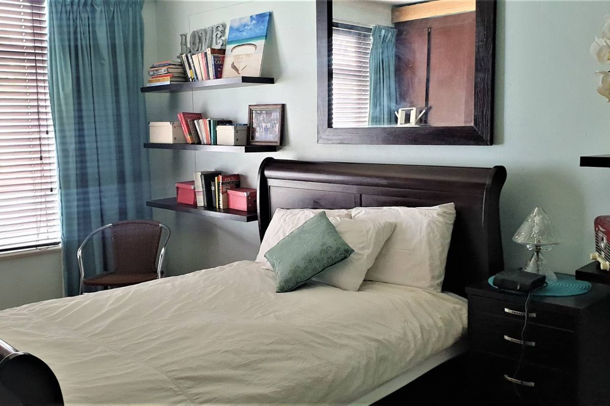 A cozy bedroom featuring light-colored walls, venetian blinds, and multiple floating shelves for storage.