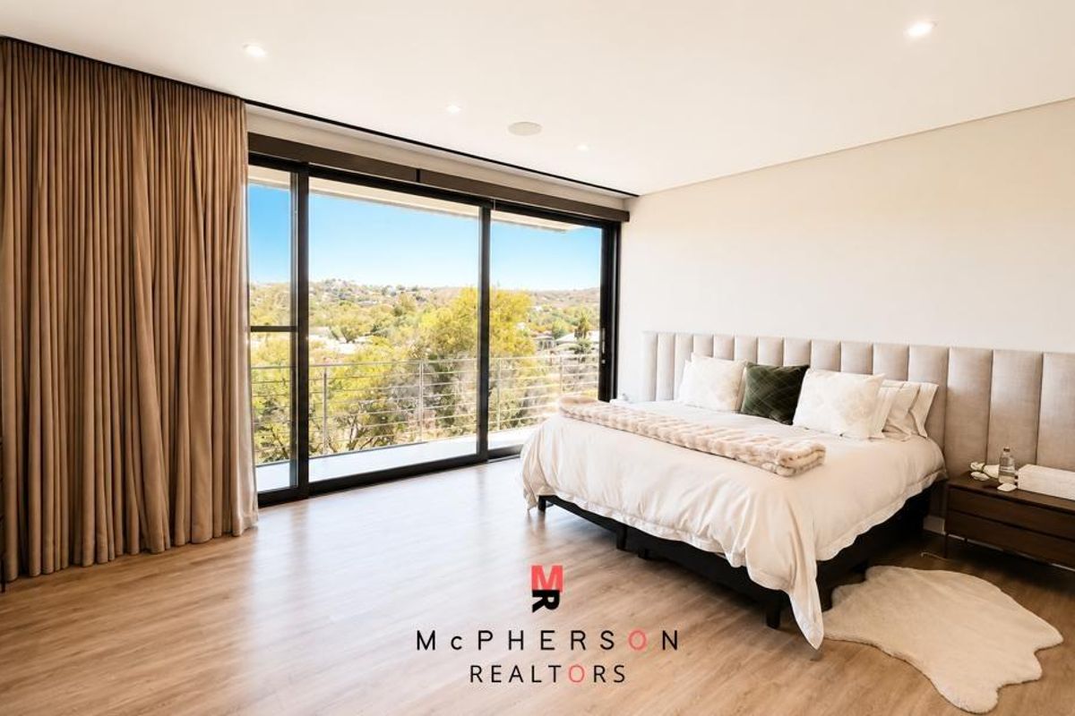 Spacious bedroom featuring modern laminate flooring, recessed lighting, and large sliding glass doors opening to a scenic balcony view.