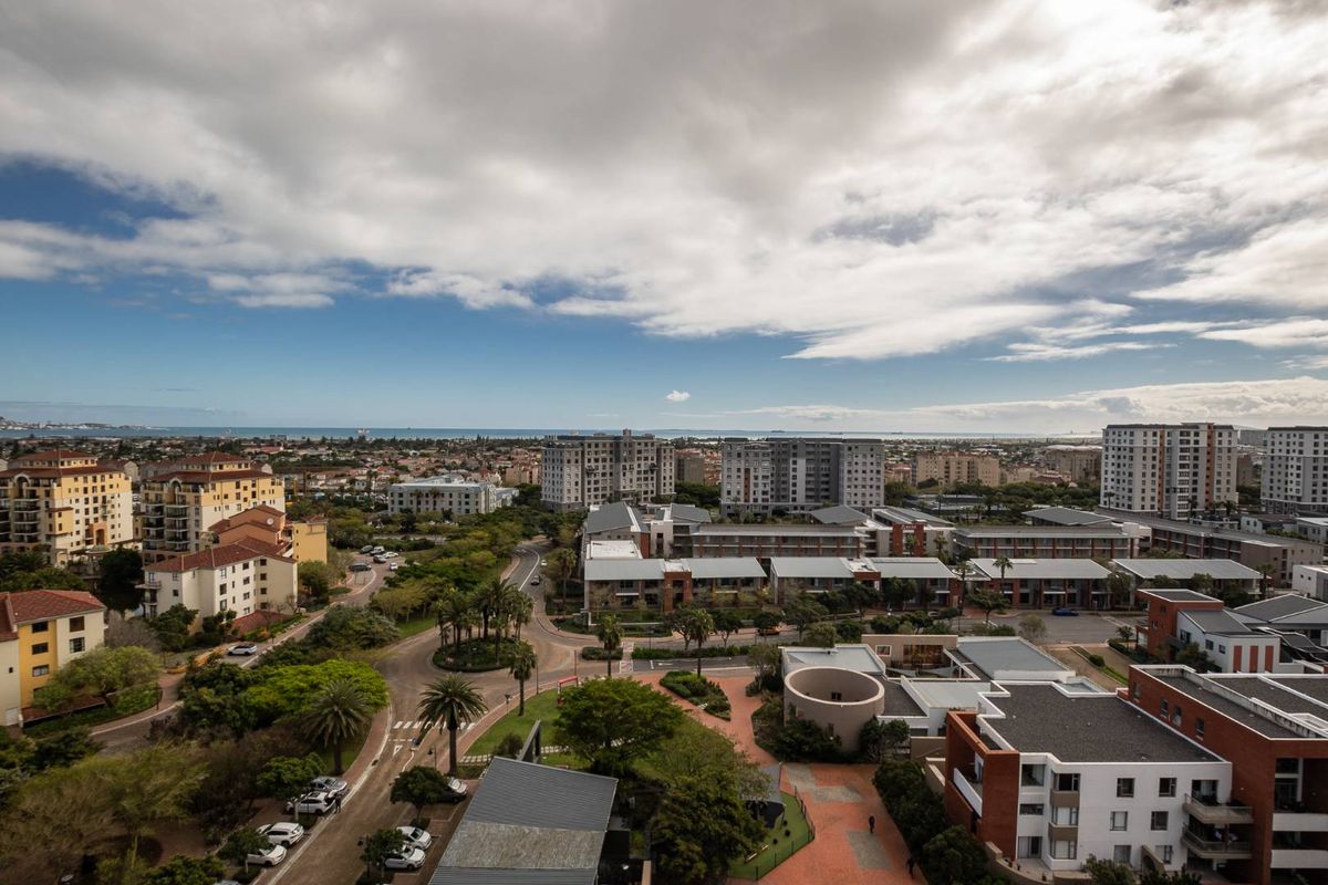 Elevated aerial view overlooking the surrounding residential apartment complex, landscaped grounds, and distant coastal horizon.